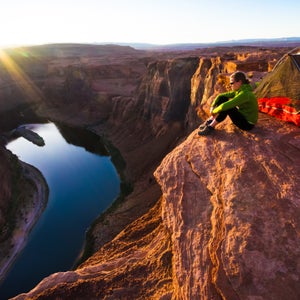 A woman sitting next to her tent overlooks the Colorado River in Arizona as the sun sets