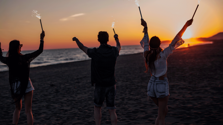 Young people on a beach at sunset taking part in a moon circle