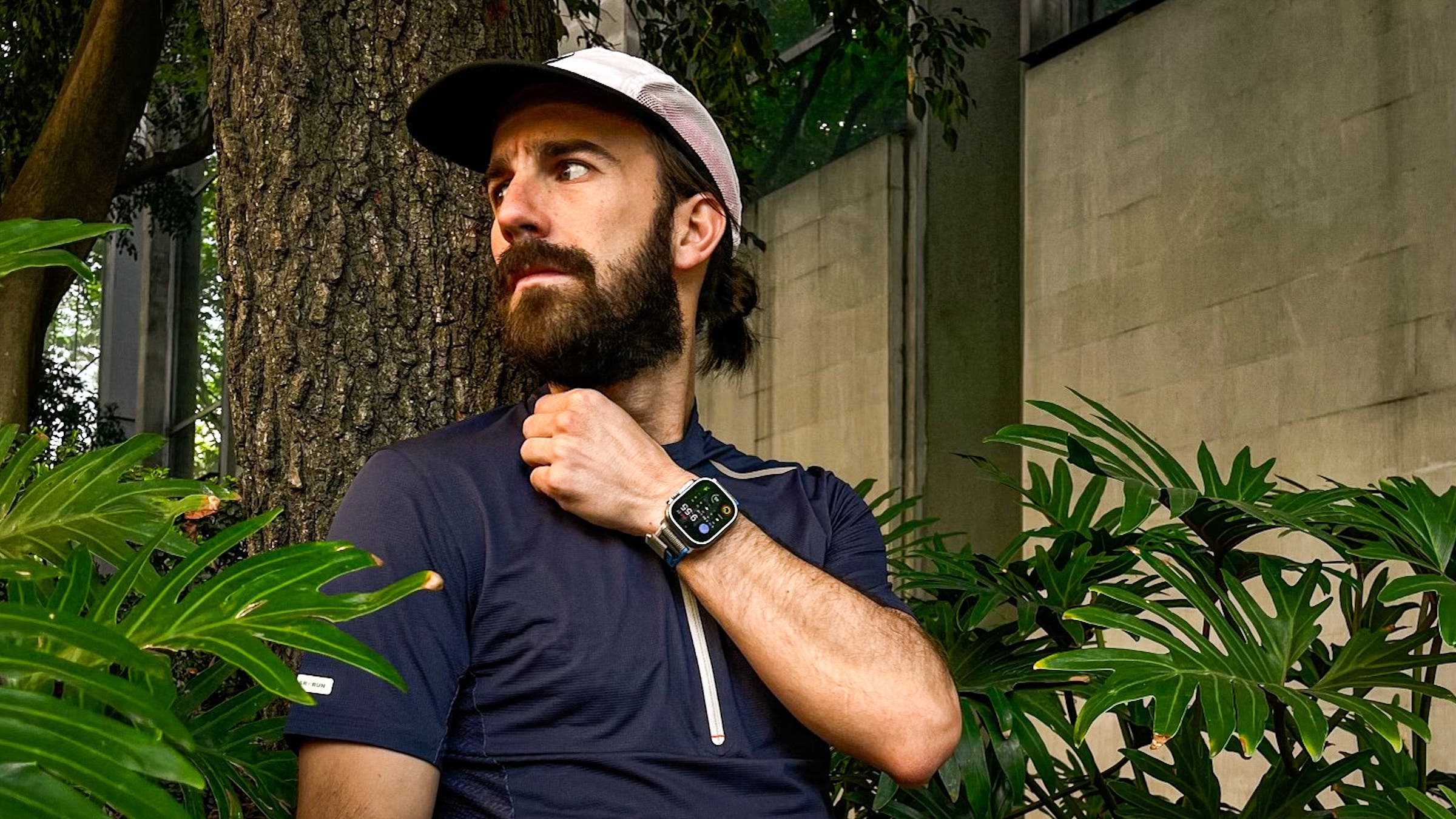 The owner of the running store in a black shirt and white hat looks to the left with a watch