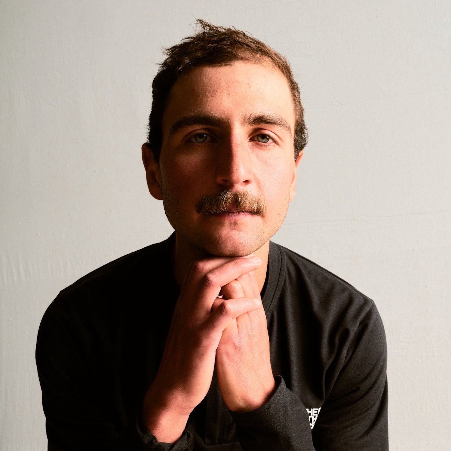 man with a black shirt and a mustache in front of a white backdrop