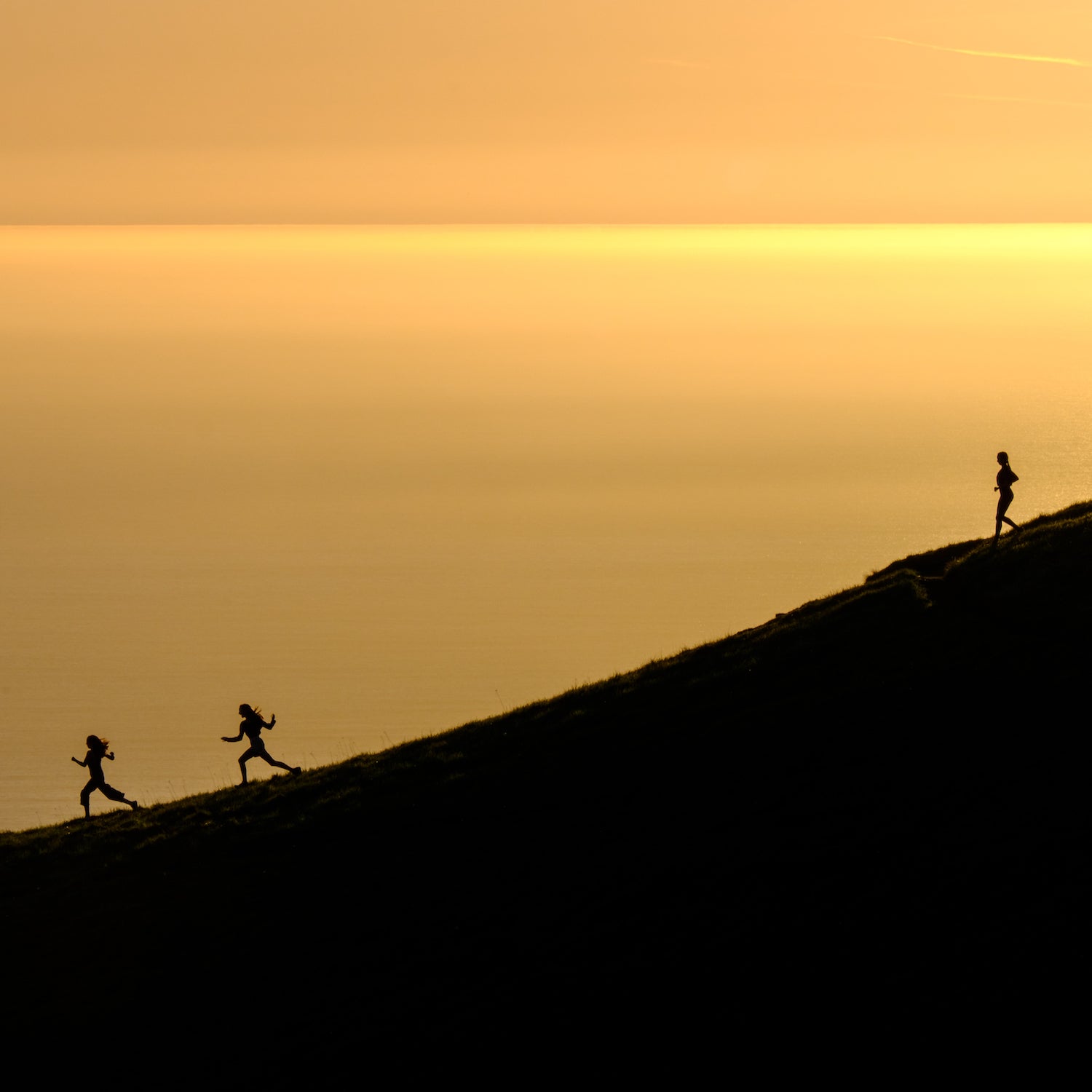 Three girls running down a slope near the ocean