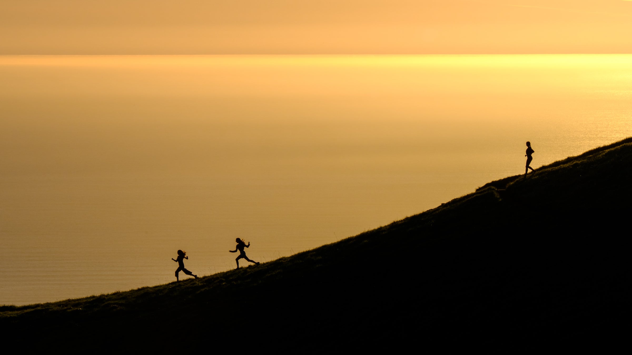 Three girls running down a slope near the ocean