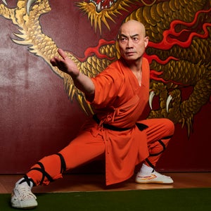 Man in orange kung fu outfit poses on a green mat