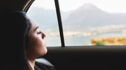 Person looks out the window of a car at a view of distant mountains.