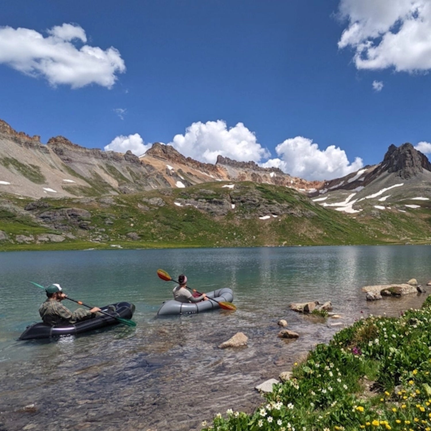 Two people in boats are floating on a high alpine lake