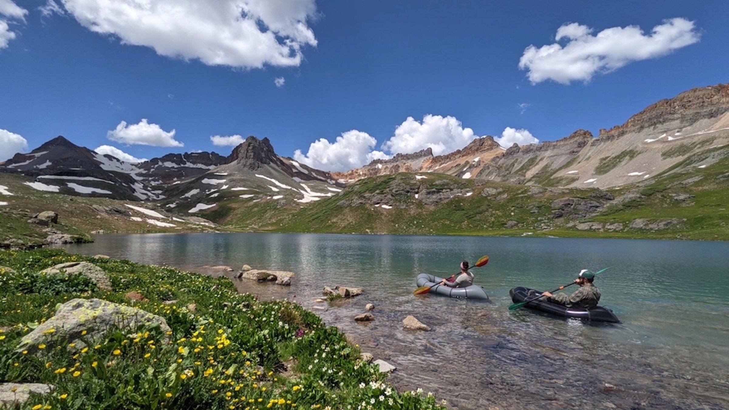 Two people in boats are floating on a high alpine lake