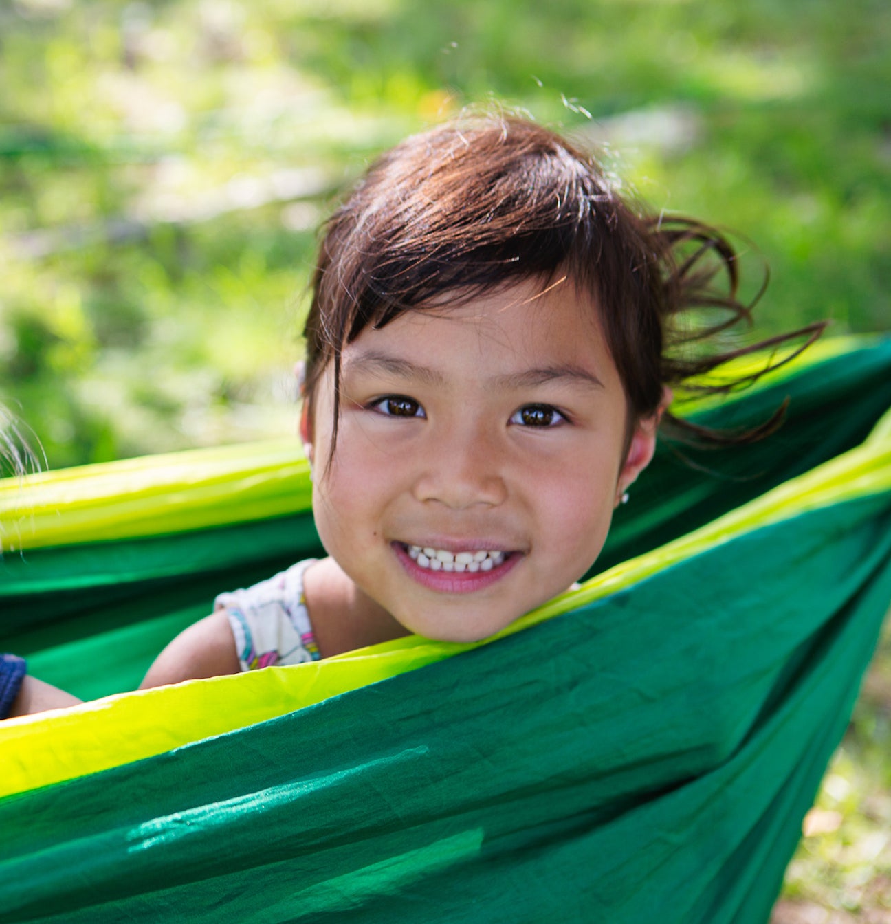 Smiling sisters sitting in green hammock at camp ground