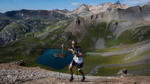Courtney Dauwalter hikes in the mountains with a blue lake in the background and mountains