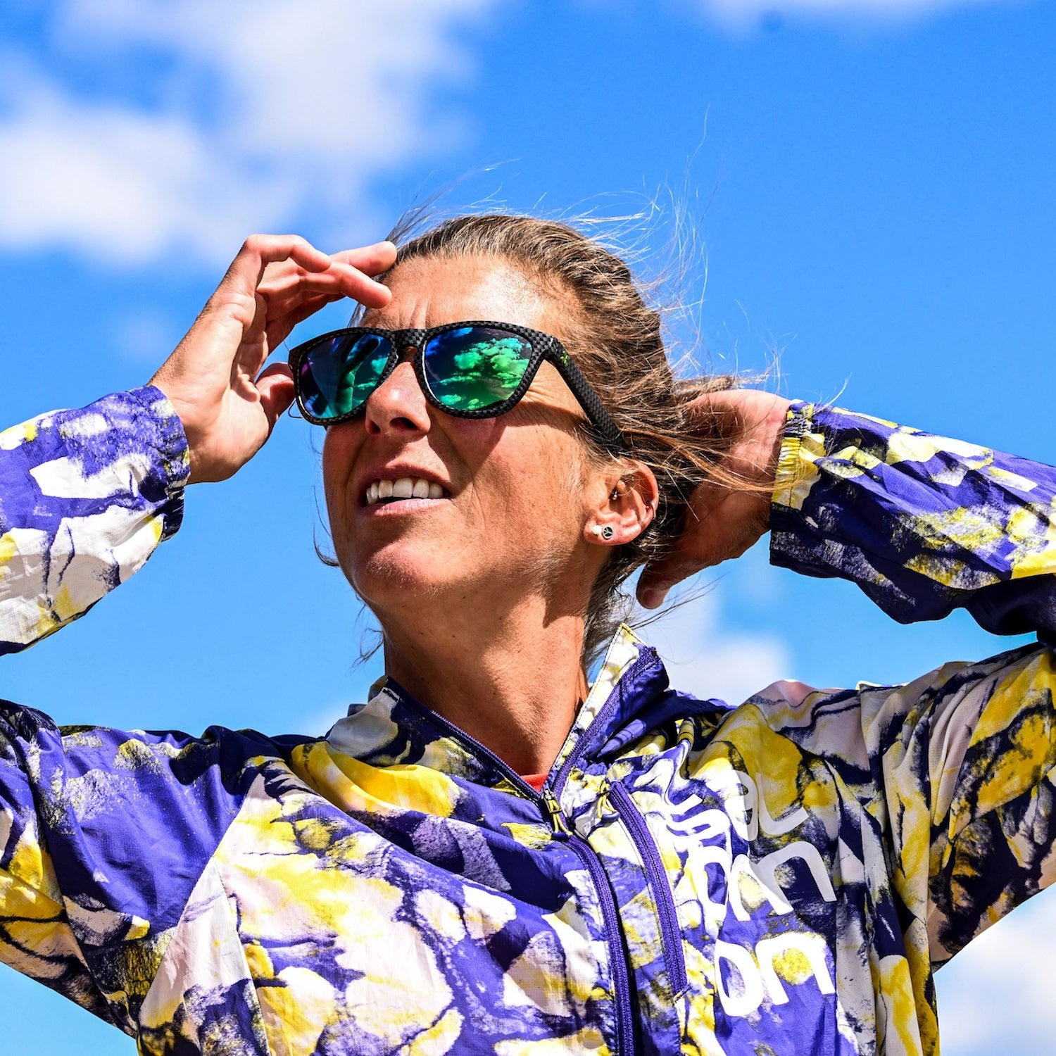 Ultrarunner in a purple and yellow jacket in sunglasses with a blue sky backdrop