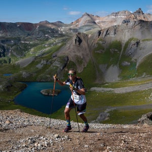 Woman hikes in the mountains with a blue lake in the background and mountains
