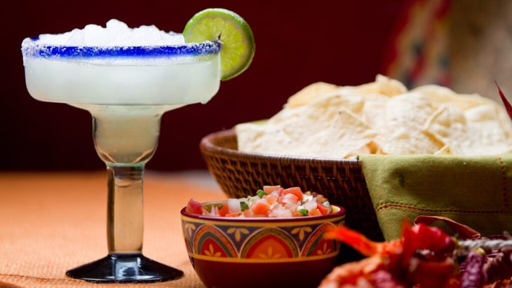 A frozen margarita with lime next to bowls of fresh salsa and chips