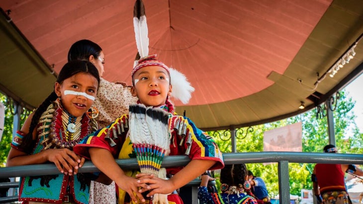 Two Native girls in feathers and beaded outfits wait to dance at Santa Fe's Indian Market.