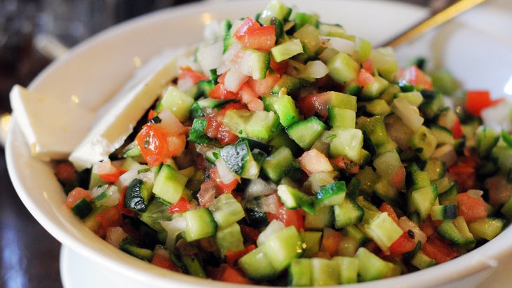 A view of Israeli salad (cucumbers, tomatoes and herbs) in a white bowl.
