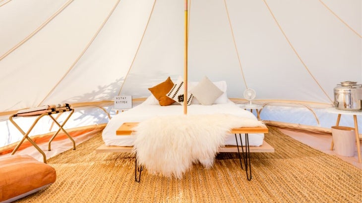 The interior of a white tent shows a queen bed with two pillows and a sheepskin run on a bench