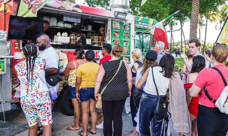 Thirteen people waiting in line for a food truck selling tacos and burritos