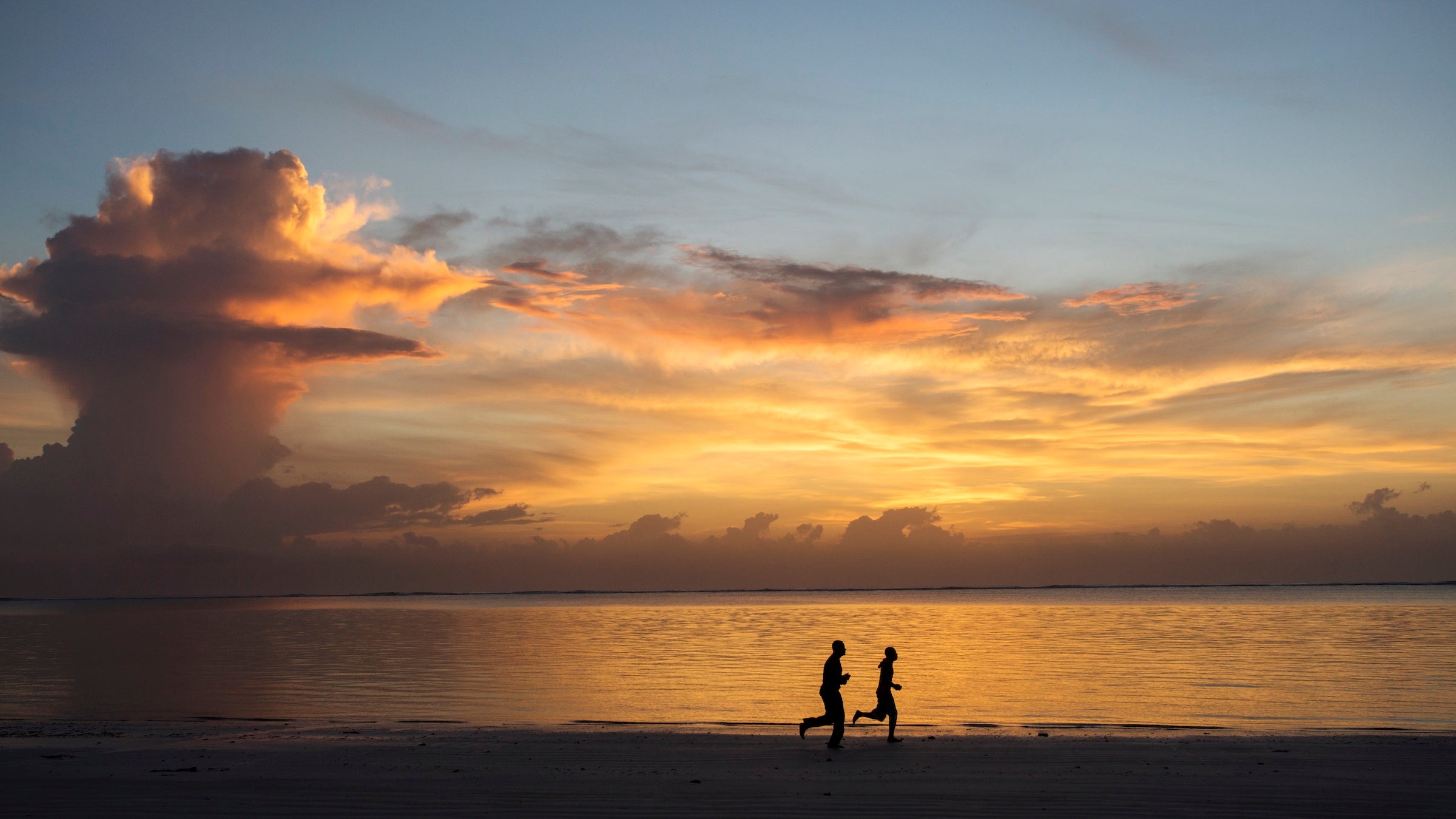 Silhouette of two people jogging on beach at sunrise