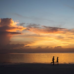 Silhouette of two people jogging on beach at sunrise