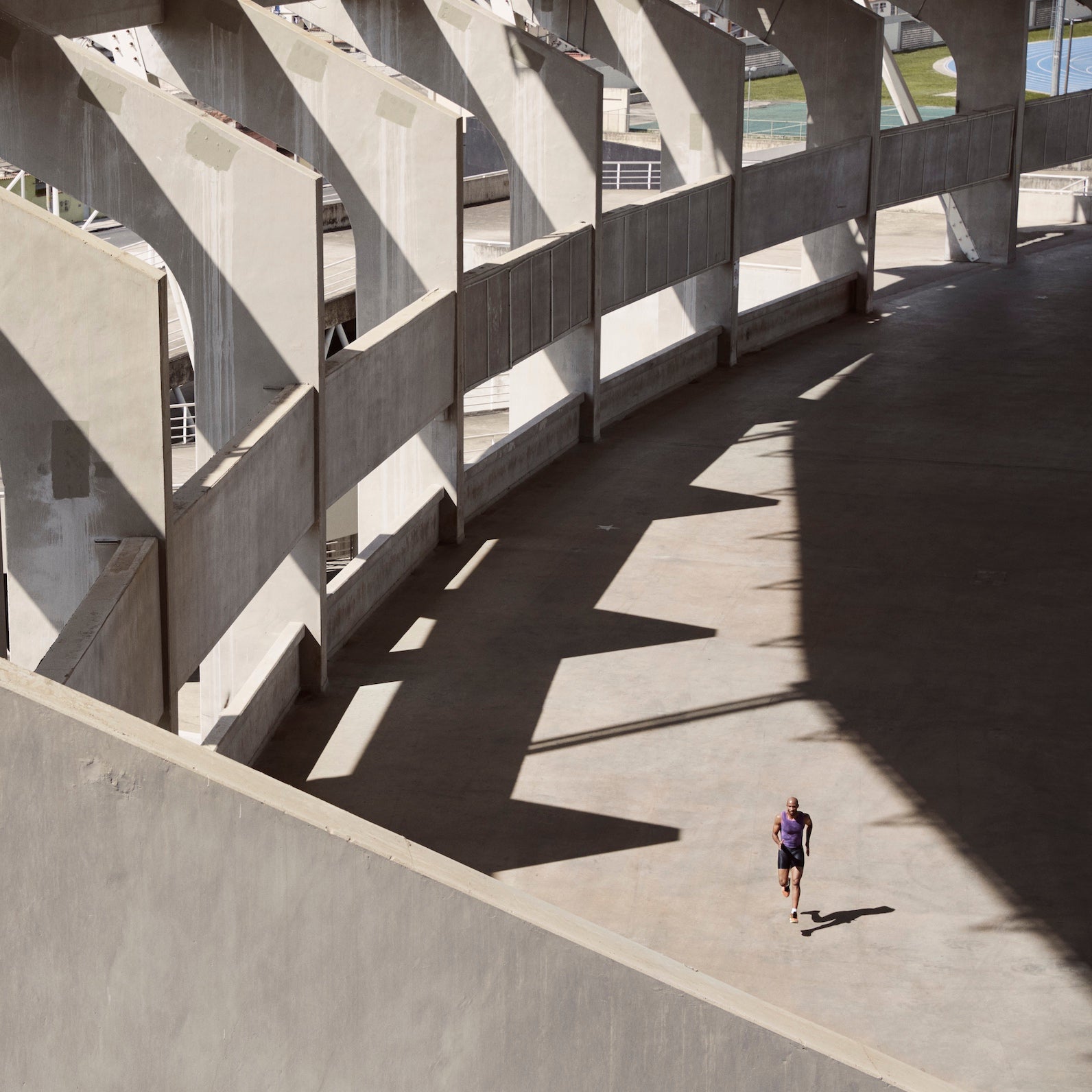 Long shot of a male athlete as he runs through a concrete stadium