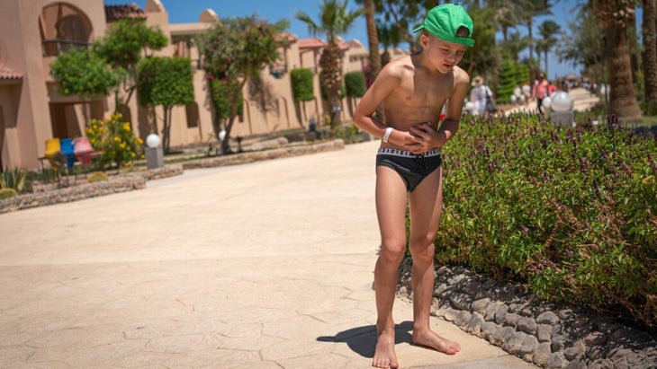 A boy in a black swimsuit clutches his stomach on the street of a vacation residence.