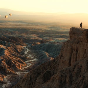 woman on cliff watches balloons over desert