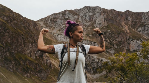 Hiker with pink hair and a backpack posing in front of mountains after getting outside to help reduce anxiety