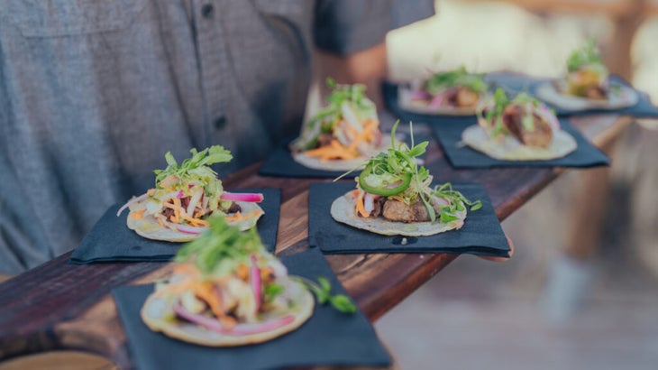 A server carries a wooden board laden with tacos