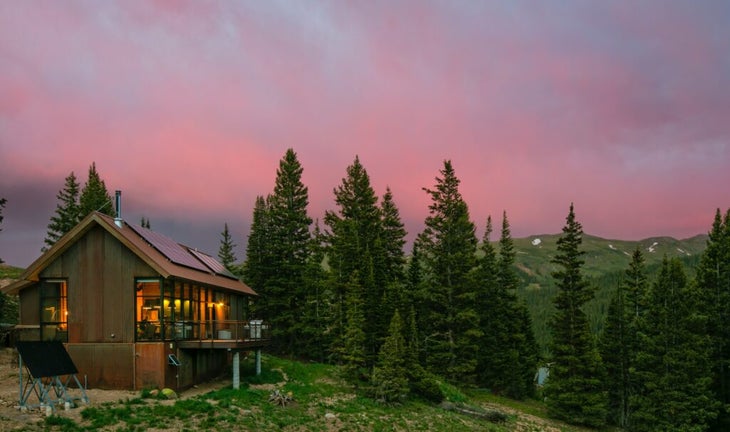 The Thelma hut perched atop a green mountain at dusk, with a sky of pink