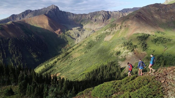 Three trail runners descending a green mountainous slope