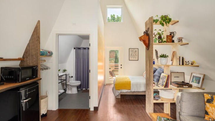 The inside of an A-frame, decorated with a queen bed, bookshelves, a mini fridge, and a record player