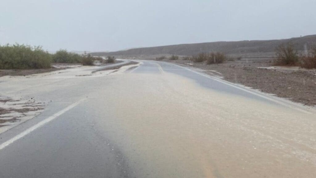 Muddy water flows across a paved road in a desert landscape.