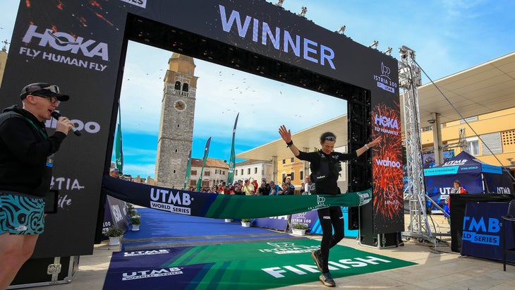 A man in all black runs through a finish line in first place