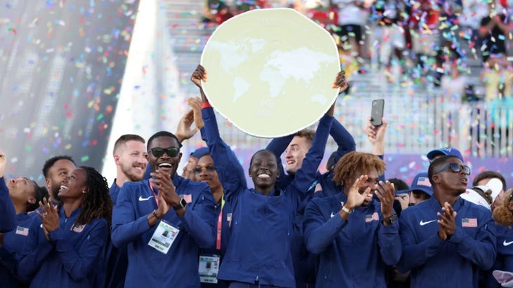 Team USA wearing blue together holds up a big gold medal and smiles