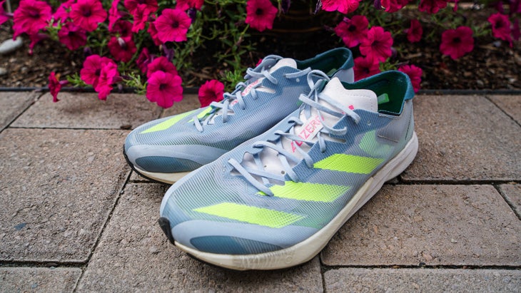 A running shoe with green stripes in front of red flowers in the background