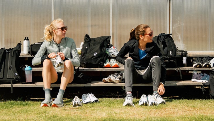 Two women elite runners sit on a bench and get ready to run