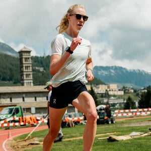 A woman runs around a track with black sunglasses and a green-blue shirt