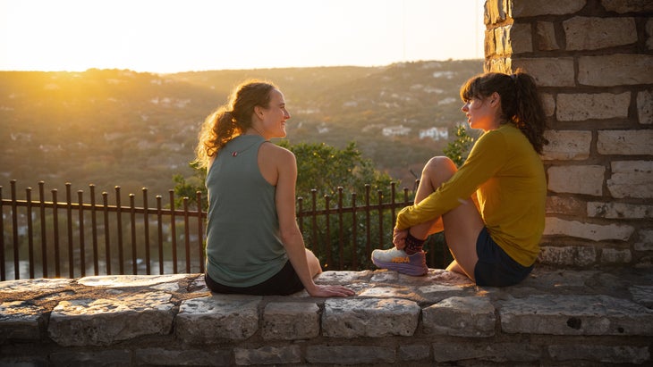 two women talking at sunset on a rock wall