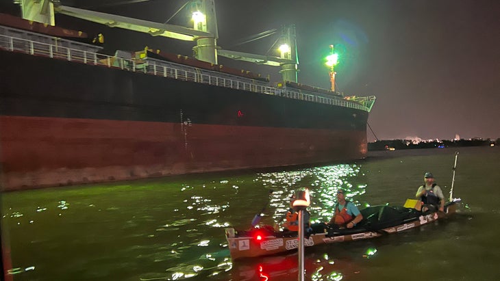 A canoe crew paddles past an ocean liner 