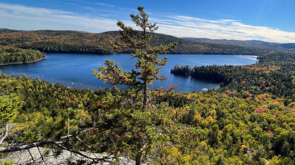 A clifftop view of a cobalt-blue Debsconeag Lake surrounded by the forest
