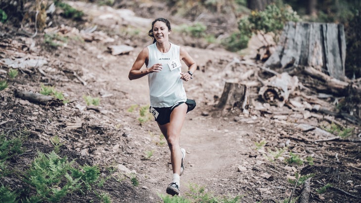 a woman in a white shirt smiles while running trails