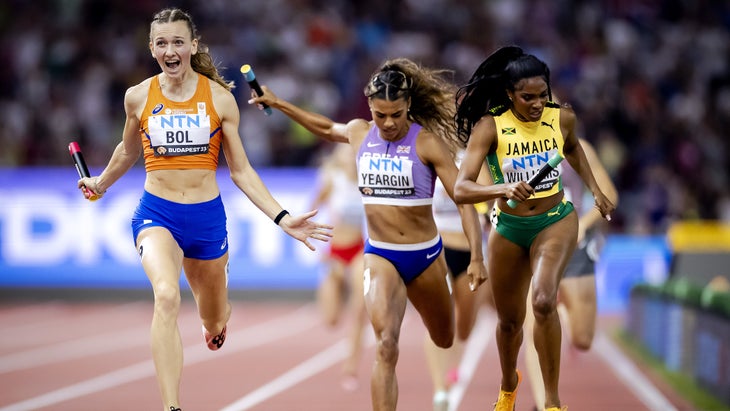 A woman in orange outfit wins a relay race with two other women close behind