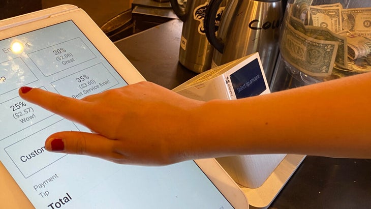 A girl taps on the 25 percent option on an electric screen prompt for tipping