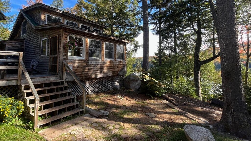 A wooden camp structure named "Harrison Camp," with potted flowers hanging from the roof
