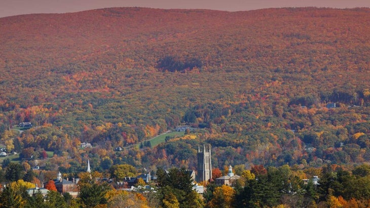 The cathedral of historic Williamstown, Massachusetts rises above a mountain covered in red, yellow, and green fall foliage