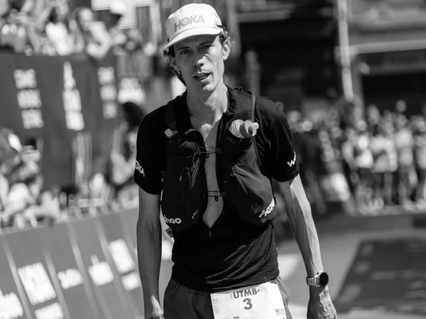 A runner in a white hat and black shirt at the finish line of a 100 mile race