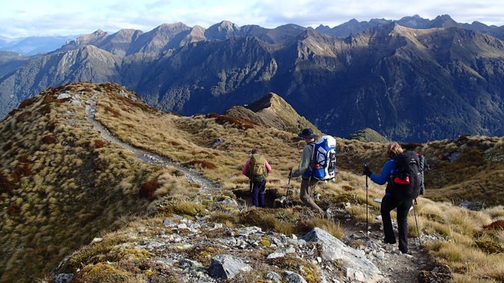 Three hikers top out on a high section of New Zealand's Kepler Track, with incredible views of the surrounding peaks