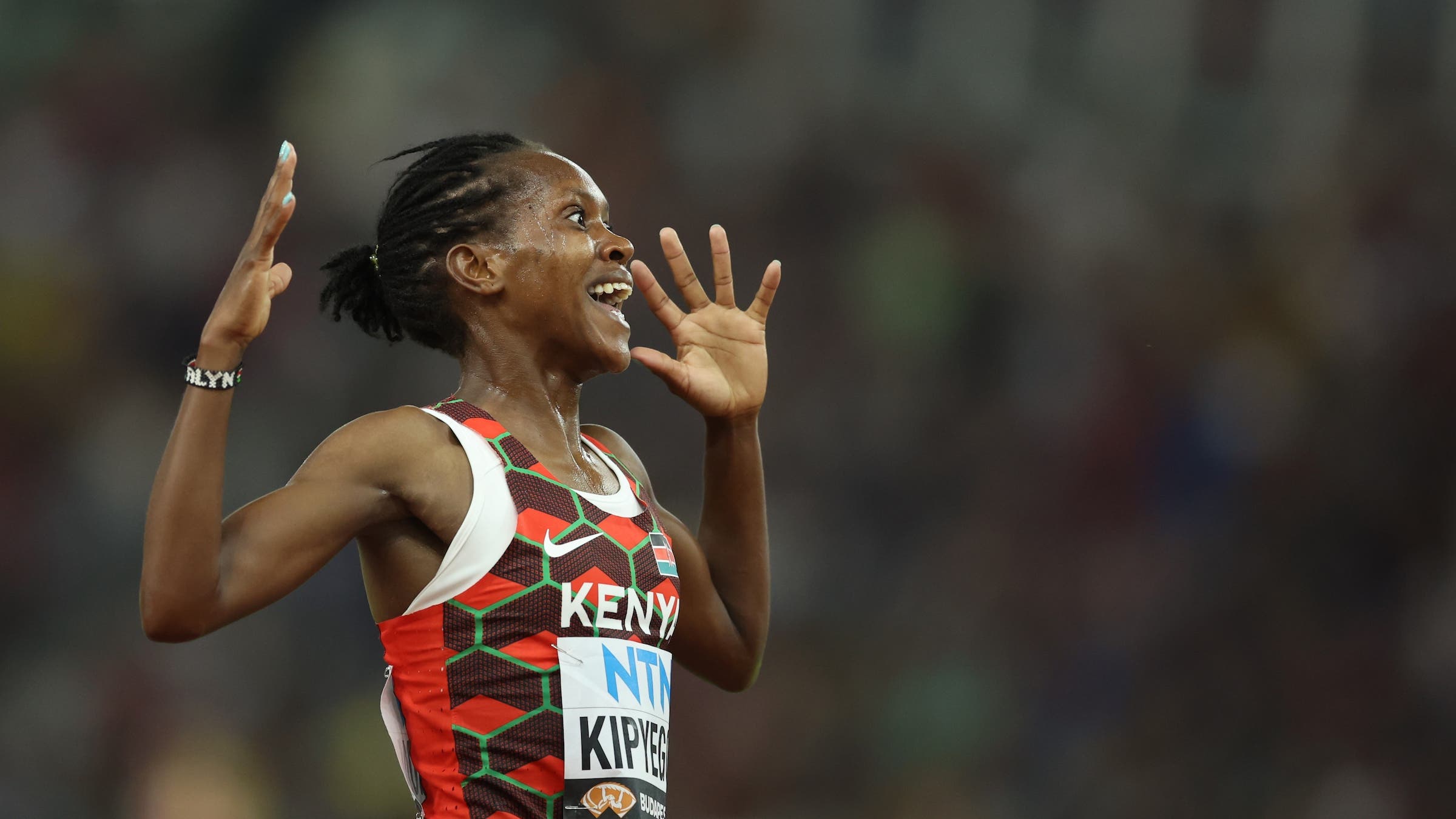 A track star celebrates in a red singlet after winning a race