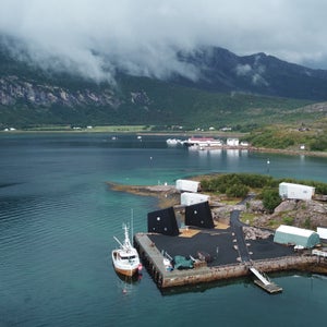 Manshausen Island, surrounded by turquoise waters and cloud-covered mountains in the distance