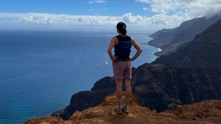 A sporty-looking woman standing on a bluff looking over the Na Pali coast and Pacific Ocean