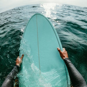 First person point of view photo of a surfer floating in the ocean while catching the waves on his surfboard