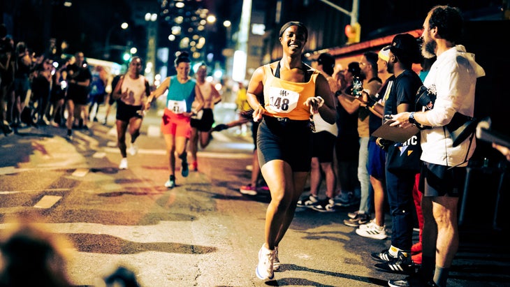 A woman smiles wearing orange and running at night in the city